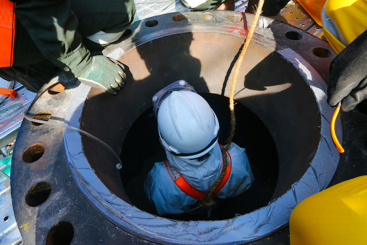 Man in hard hat enters man hole in confined space safety training.