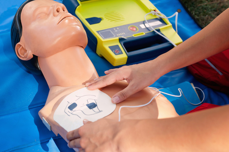 Woman attaches defibrillator to CPR manikin in CPR / AED class.